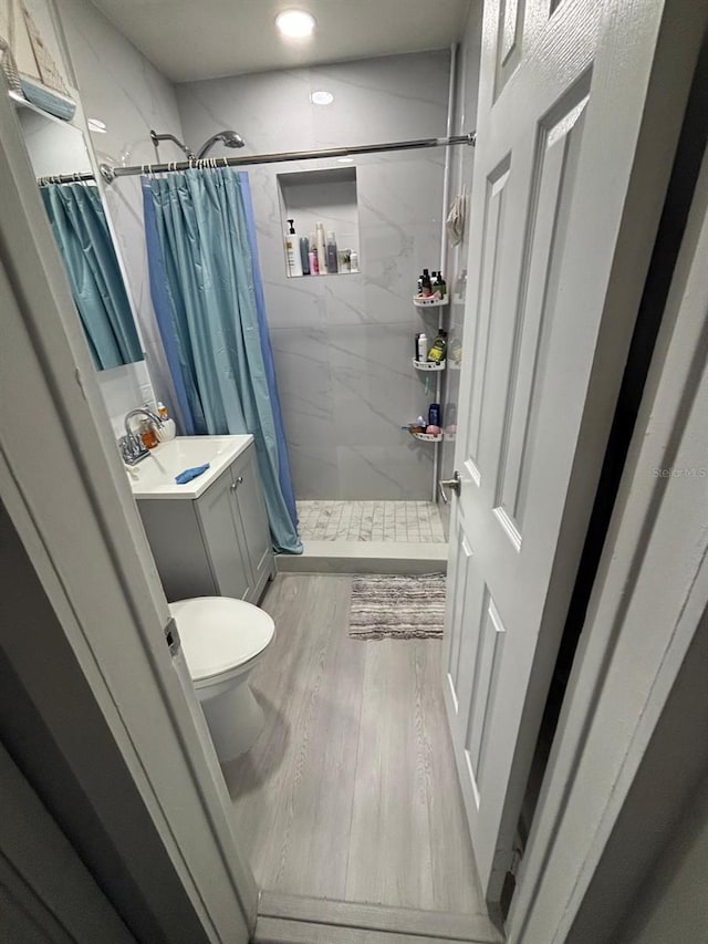 bathroom with hardwood / wood-style floors, vanity, toilet, and curtained shower