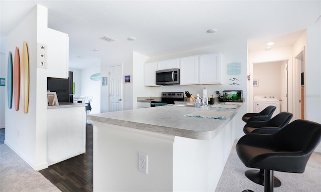 kitchen with a kitchen breakfast bar, kitchen peninsula, appliances with stainless steel finishes, white cabinetry, and washer / clothes dryer