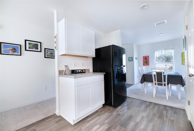 kitchen featuring pendant lighting, an inviting chandelier, white cabinets, black refrigerator, and light wood-type flooring