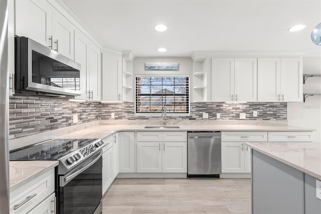 kitchen with light stone countertops, appliances with stainless steel finishes, backsplash, sink, and white cabinets