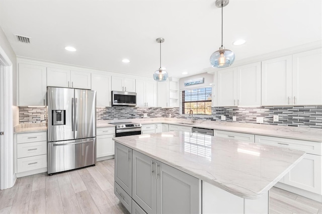 kitchen featuring light stone countertops, stainless steel appliances, decorative light fixtures, a center island, and white cabinetry