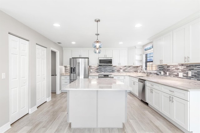 kitchen featuring appliances with stainless steel finishes, light wood-type flooring, pendant lighting, white cabinets, and a center island