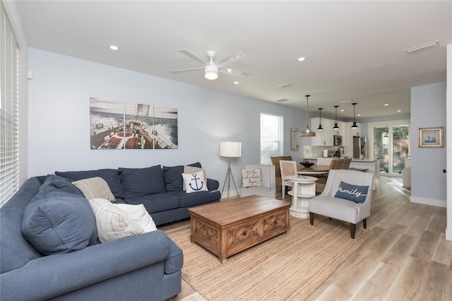 living room featuring light hardwood / wood-style flooring, ceiling fan, and a healthy amount of sunlight