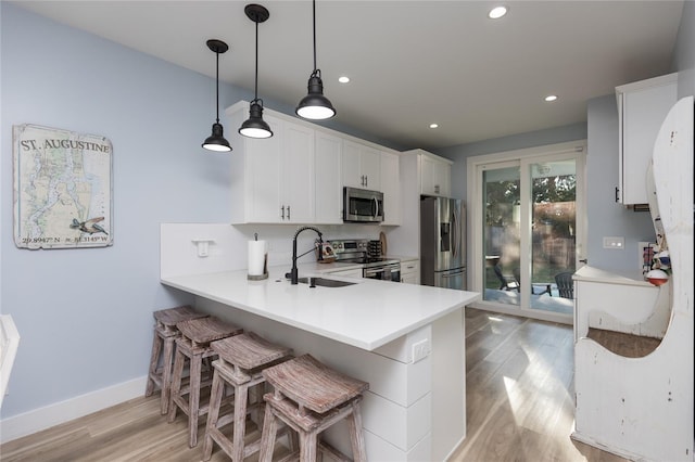 kitchen with white cabinets, sink, appliances with stainless steel finishes, kitchen peninsula, and a breakfast bar area