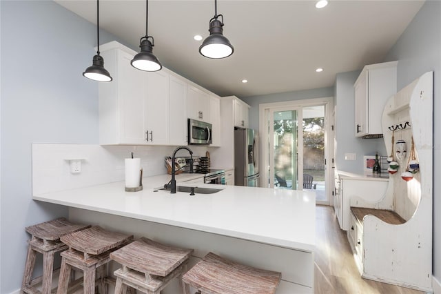 kitchen with kitchen peninsula, appliances with stainless steel finishes, a kitchen breakfast bar, pendant lighting, and white cabinetry