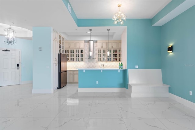 kitchen with stainless steel refrigerator, hanging light fixtures, wall chimney range hood, a notable chandelier, and decorative backsplash