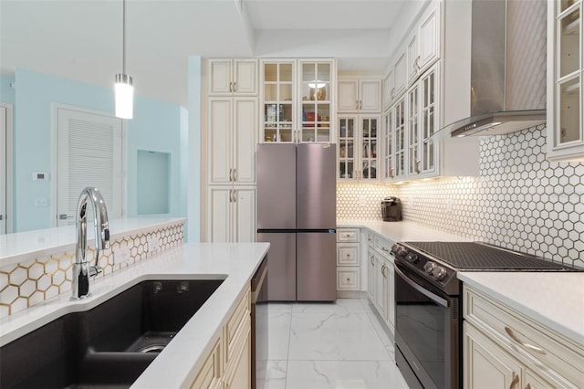 kitchen featuring sink, wall chimney exhaust hood, stainless steel appliances, cream cabinets, and decorative light fixtures