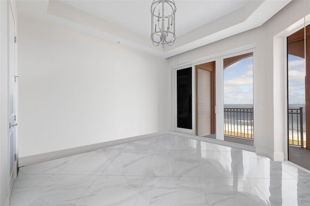 empty room with an inviting chandelier, a water view, and a tray ceiling