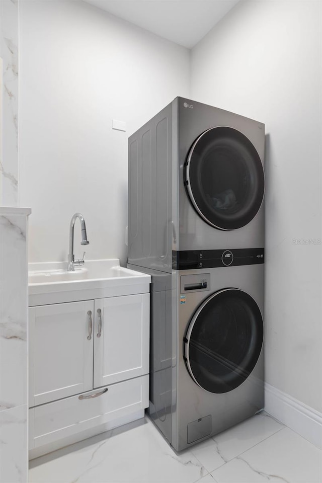 clothes washing area featuring cabinets, sink, and stacked washing maching and dryer