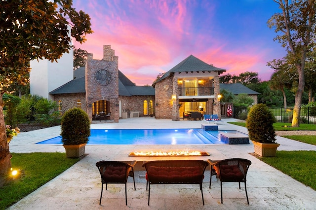 pool at dusk featuring a fire pit, a hot tub, and a patio