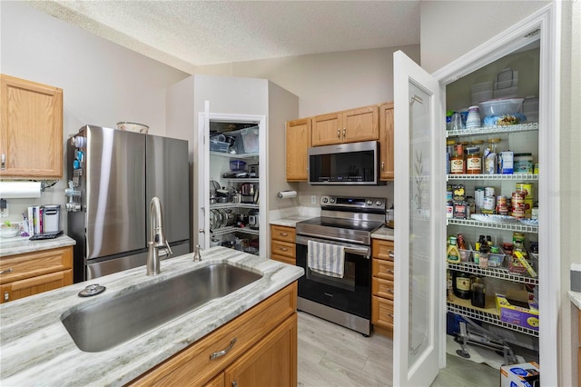 kitchen featuring sink, a textured ceiling, light hardwood / wood-style floors, light stone counters, and stainless steel appliances