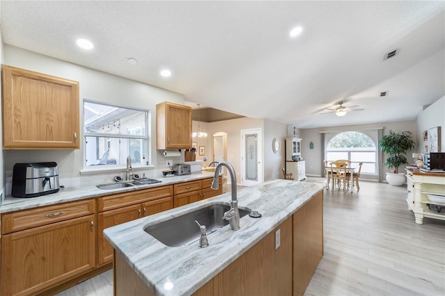 kitchen featuring light stone countertops, a center island, ceiling fan with notable chandelier, and sink