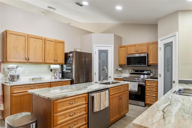 kitchen featuring appliances with stainless steel finishes, light wood-type flooring, a textured ceiling, a kitchen island with sink, and sink