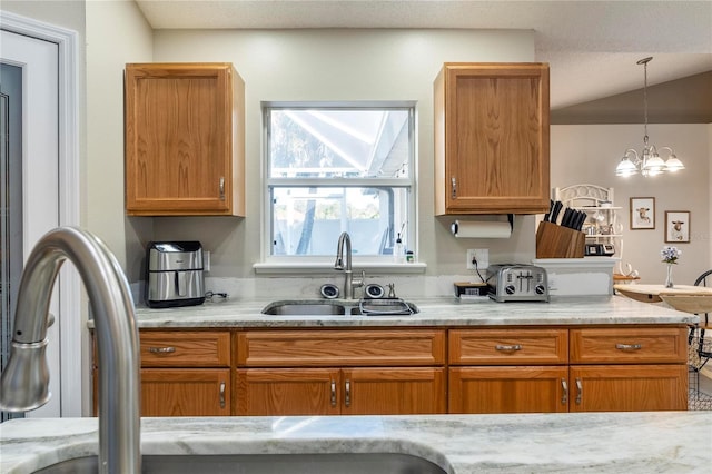 kitchen with pendant lighting, light stone counters, sink, and a chandelier