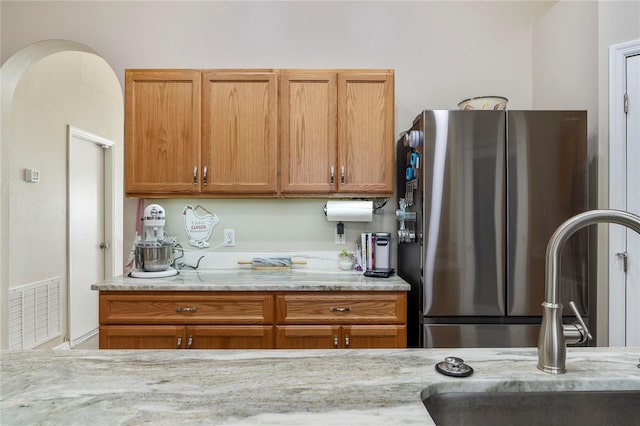 kitchen featuring stainless steel refrigerator, light stone countertops, and sink