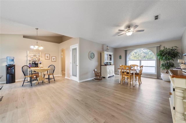 dining space featuring a textured ceiling, ceiling fan with notable chandelier, light hardwood / wood-style flooring, and lofted ceiling