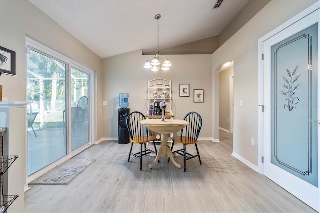 dining area with light hardwood / wood-style floors, lofted ceiling, a textured ceiling, and an inviting chandelier