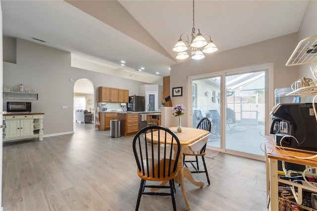 dining room with light wood-type flooring, vaulted ceiling, and an inviting chandelier