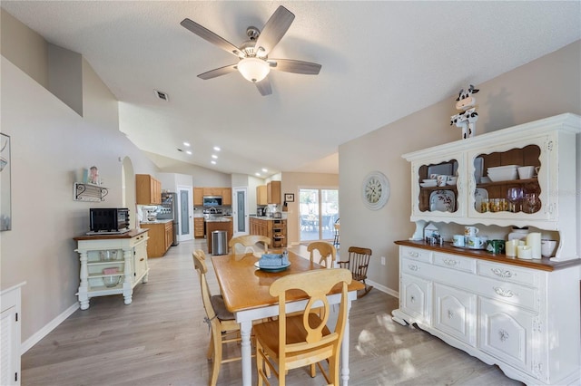 dining room with ceiling fan, light wood-type flooring, a textured ceiling, and vaulted ceiling