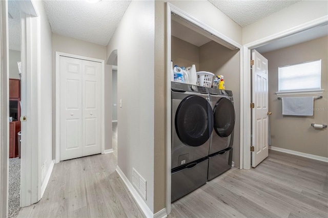 clothes washing area featuring light hardwood / wood-style floors, washing machine and dryer, and a textured ceiling