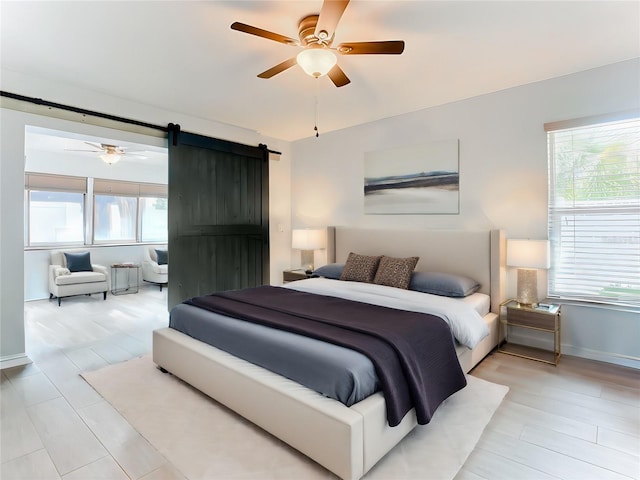 bedroom featuring ceiling fan, a barn door, light hardwood / wood-style flooring, and multiple windows