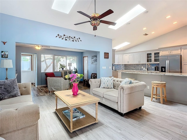 living room with vaulted ceiling with skylight, ceiling fan, and light hardwood / wood-style flooring