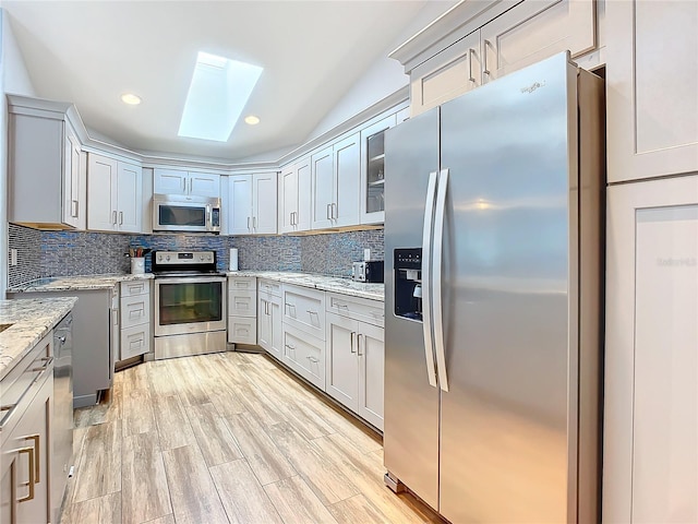 kitchen featuring backsplash, light stone countertops, light hardwood / wood-style flooring, and stainless steel appliances