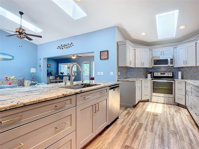 kitchen featuring light stone counters, gray cabinetry, stainless steel appliances, ceiling fan, and sink