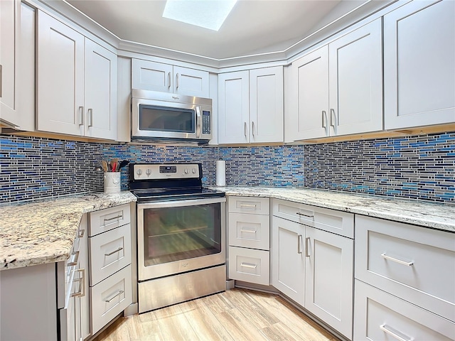 kitchen featuring light stone countertops, appliances with stainless steel finishes, backsplash, and a skylight