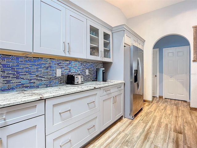 kitchen featuring tasteful backsplash, light stone countertops, light hardwood / wood-style floors, and stainless steel refrigerator with ice dispenser