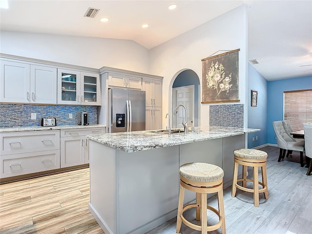 kitchen featuring sink, a kitchen breakfast bar, backsplash, stainless steel fridge, and vaulted ceiling