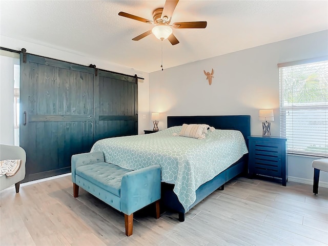 bedroom featuring a barn door, ceiling fan, and light wood-type flooring