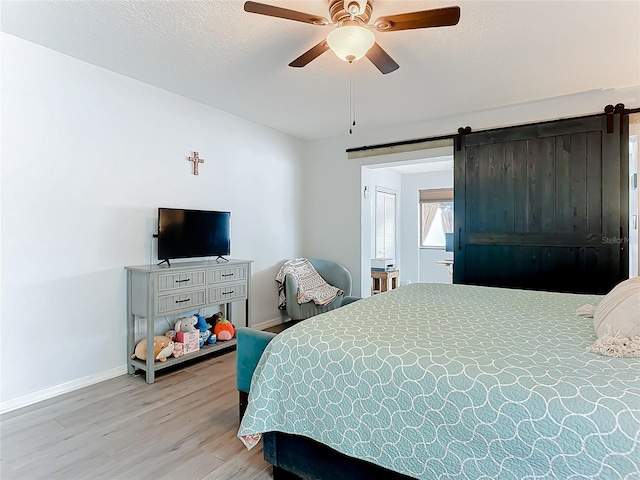 bedroom featuring ceiling fan, a barn door, a textured ceiling, and light hardwood / wood-style flooring