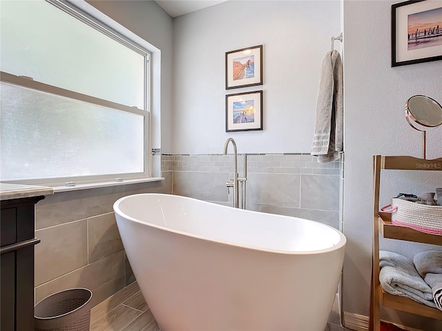 bathroom with a healthy amount of sunlight, vanity, tile walls, and a bathing tub