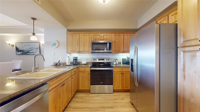 kitchen featuring decorative backsplash, appliances with stainless steel finishes, sink, decorative light fixtures, and light hardwood / wood-style flooring