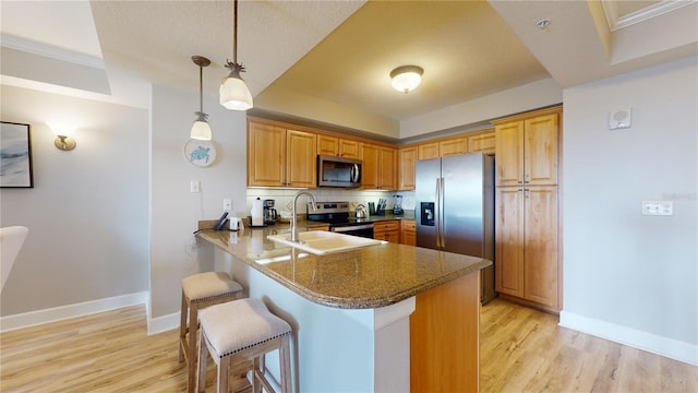 kitchen with kitchen peninsula, appliances with stainless steel finishes, light wood-type flooring, sink, and decorative light fixtures