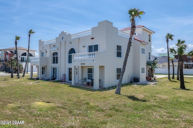 back of property with central AC unit, a balcony, and a yard