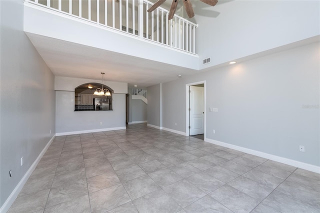 unfurnished living room featuring light tile patterned floors, a towering ceiling, and ceiling fan with notable chandelier