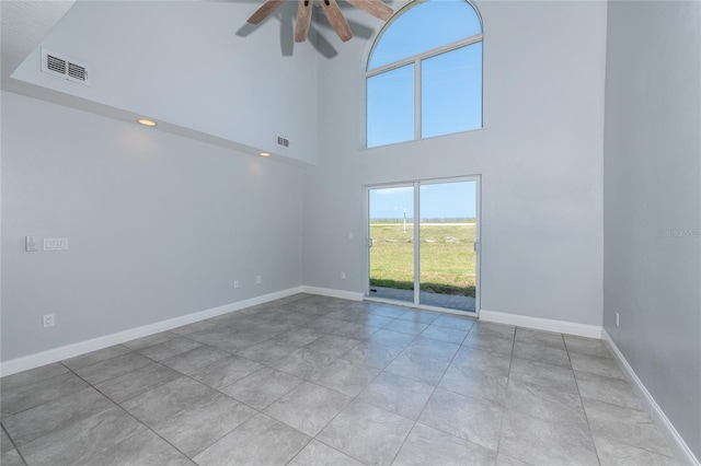 empty room featuring ceiling fan, a high ceiling, and light tile patterned floors