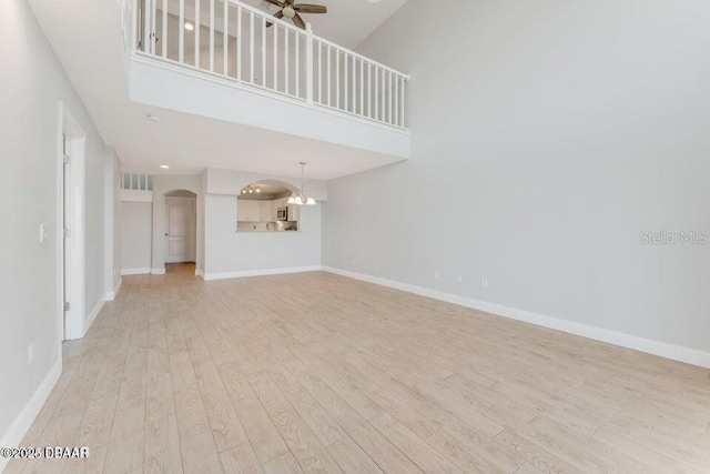 unfurnished living room with ceiling fan, a towering ceiling, and light hardwood / wood-style floors