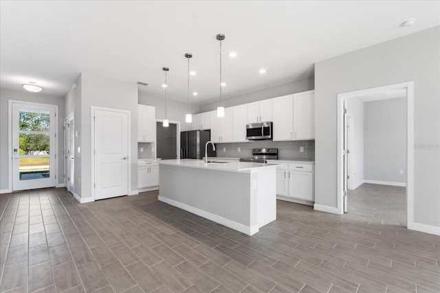 kitchen with appliances with stainless steel finishes, sink, white cabinetry, hanging light fixtures, and an island with sink