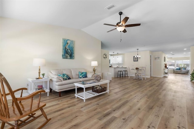 living room featuring ceiling fan with notable chandelier, light wood-type flooring, and vaulted ceiling