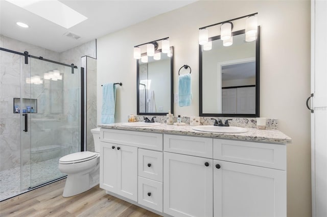 bathroom featuring a skylight, toilet, vanity, a shower with shower door, and hardwood / wood-style flooring