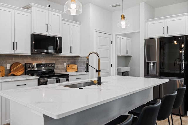 kitchen with white cabinetry, sink, decorative light fixtures, a center island with sink, and appliances with stainless steel finishes