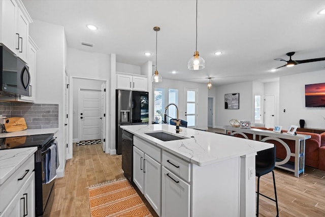 kitchen with sink, a center island with sink, white cabinets, black appliances, and light wood-type flooring