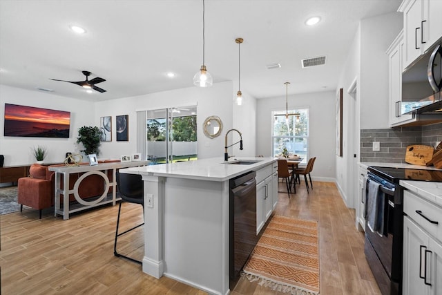 kitchen with black appliances, sink, decorative light fixtures, a center island with sink, and white cabinets