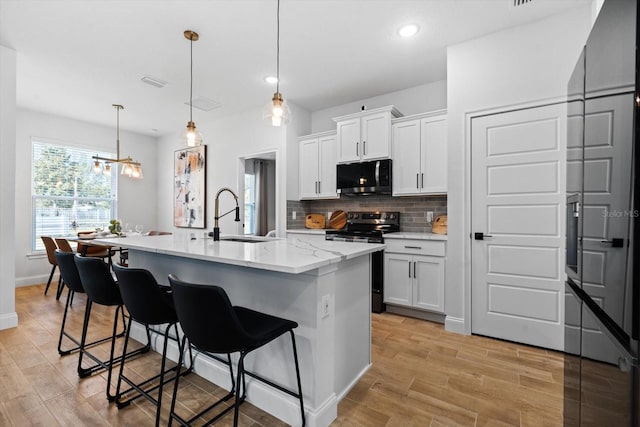 kitchen featuring white cabinetry, a center island with sink, pendant lighting, and stainless steel range with electric stovetop