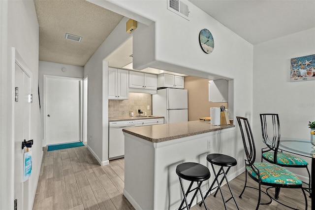 kitchen featuring white appliances, backsplash, white cabinets, sink, and light hardwood / wood-style floors