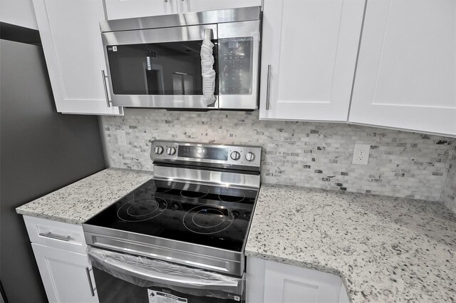 kitchen with white cabinets, appliances with stainless steel finishes, backsplash, and light stone countertops