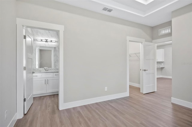 unfurnished bedroom with ensuite bath, a walk in closet, a closet, and light wood-type flooring